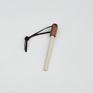 May include: A fire starter with a light-colored, cylindrical body and a wooden handle. A dark brown leather cord is attached to the handle. The fire starter is designed for outdoor use and survival.