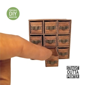 May include: A miniature wooden cabinet with nine drawers, one of which is open. The cabinet has metal handles and is labeled "Printable DIY miniature" and "Straight Outta Printer". The cabinet is brown.
