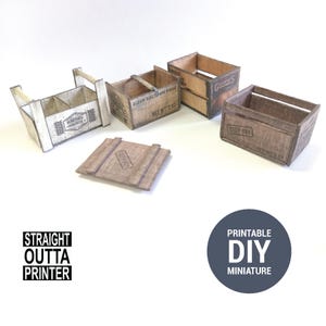 May include: A collection of miniature wooden crates and a lid, with printed text and designs. One crate has a handle and is painted white. The text "STRAIGHT OUTTA PRINTER" and "PRINTABLE DIY MINIATURE" are also visible.
