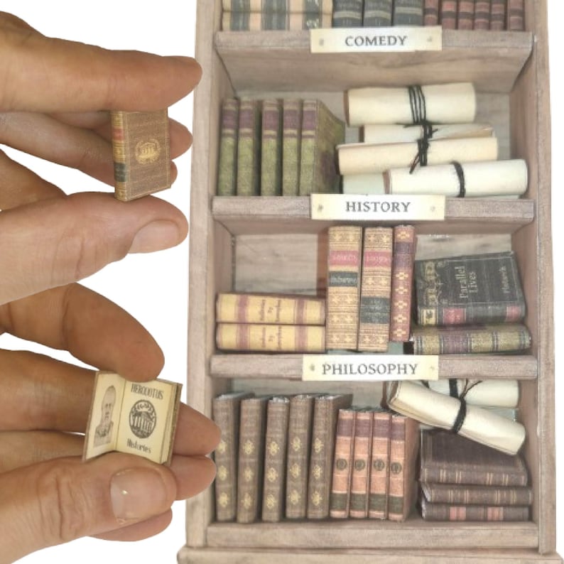 May include: Miniature wooden bookshelf filled with tiny books and scrolls. The shelves are labeled "COMEDY", "HISTORY", and "PHILOSOPHY". A small book is held in a person's hand, open to a page with text and an illustration.