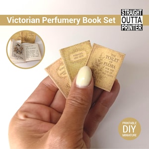 Pode incluir: Um conjunto de livros de perfumaria vitoriana em miniatura. Os livros têm texturas de papel envelhecido e títulos como "Pomades and Oils" e "The Toilet of Flora". A imagem também inclui o texto "Victorian Perfumery Book Set" e "Straight Outta Printer".