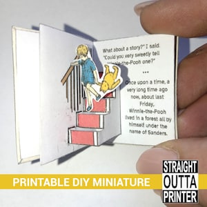 Puede incluir: Un libro de papel en miniatura con una escena emergente que presenta a Winnie the Pooh y Christopher Robin en unas escaleras. El texto dice "Winnie-the-Pooh" y "Érase una vez". La parte inferior de la imagen tiene el texto "PRINTABLE DIY MINIATURE".