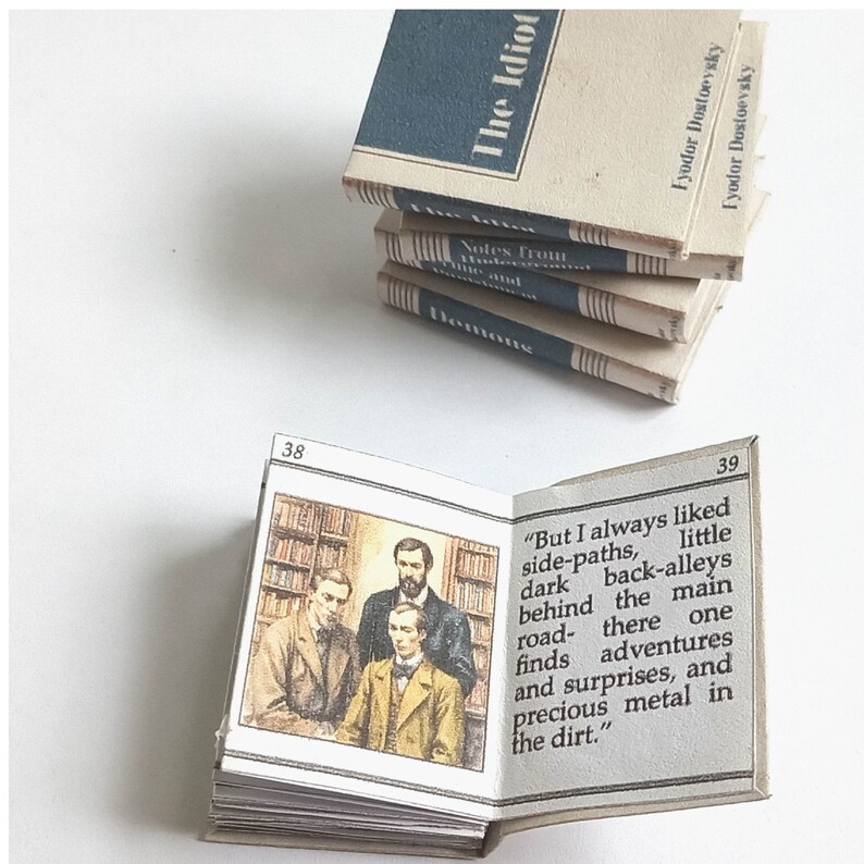 May include: An open book with a black and white illustration of three men. The text on the page reads "But I always liked side-paths, dark back-alleys behind the main road- there one finds adventures and surprises, and precious metal in the dirt."