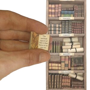 May include: A miniature bookshelf filled with tiny books, labeled "Tragedy", "Comedy", "History", and "Philosophy". A small book with the text "The saddest aspect of life is that there is no one on" is held in a hand.
