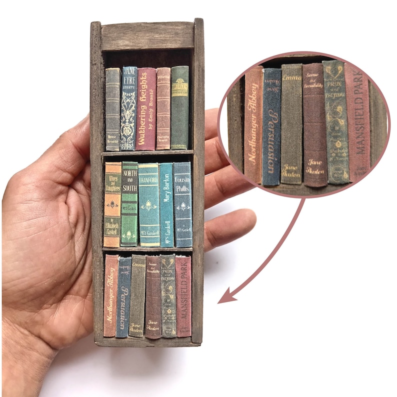 Op de afbeelding: Een miniatuur houten boekenkast met meerdere rijen miniatuurboeken. De boeken hebben titels zoals "Wuthering Heights", "Northanger Abbey", "Emma", "Pride and Prejudice" en "Mansfield Park".