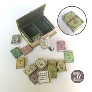 May include: A collection of miniature books with botanical illustrations and titles like "Magical Herbs," "Sage," and "Thyme." The books are in various colors, including green, pink, and yellow, and are arranged around a small, open box. The image also includes the text "Printable DIY Miniature."