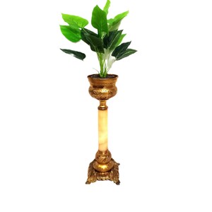 Puede incluir: Un soporte de planta de metal dorado con una parte superior redonda y tres patas. El soporte tiene una columna de mármol blanco y una planta verde en una maceta dorada.