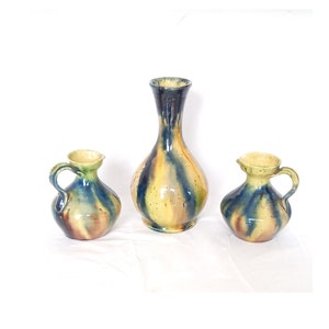 Peut inclure: Trois vases en céramique dans un glacis jaune, bleu et vert. Le vase le plus grand est un vase fin et haut avec une large ouverture. Les deux plus petits vases sont plus ronds et ont une anse.