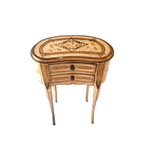 Op de afbeelding: Een kleine, ovale houten tafel met twee laden en ingelegde, ingewikkelde bloemmotieven. De tafel heeft een lichtbruine afwerking en delicate, gebogen poten.