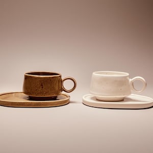 Peut inclure: Deux tasses à café en céramique avec leurs soucoupes assorties. L'une est marron et texturée, l'autre blanche et mouchetée. Les deux ont une forme arrondie et une petite anse.