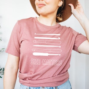 May include: A pink t-shirt with a white graphic of crochet hooks of different sizes and the text "Size Matters".
