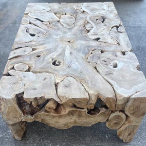 May include: A large, rustic coffee table made from a single piece of natural wood with a unique, organic shape and a light brown color.