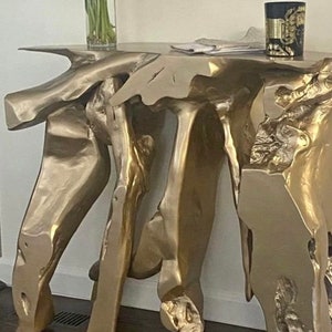 May include: A gold-colored, organic-shaped console table with a rough, textured surface. The table has a unique, asymmetrical design with multiple legs.