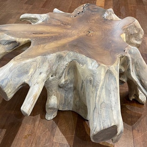 May include: A large, natural wood coffee table with a unique, organic shape. The table is made from a single piece of wood and has a natural, rustic finish.