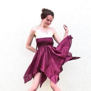 May include: A woman wearing a strapless, burgundy, asymmetrical dress with a flowing skirt. She is wearing black boots and has her hair pulled back in a bun.