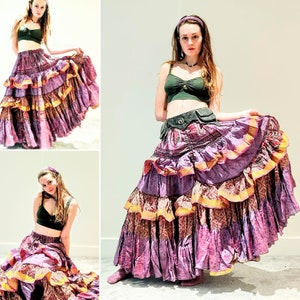 May include: A woman wearing a purple and gold layered skirt with a green crop top and a brown belt. She is posing with her arms outstretched.