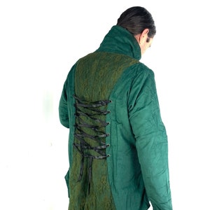 May include: A green jacket with a lace-up back detail. The jacket has a high collar and long sleeves.