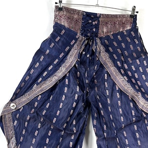 May include: Navy blue palazzo pants with a patterned design. The pants have a lace-up back and a wide leg opening. The fabric has a slight sheen. The waistband and edges are trimmed with a decorative border.