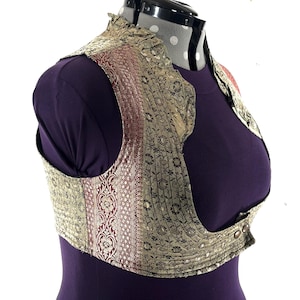 May include: A decorative vest with a floral pattern in gold and red. The vest has a high collar and a button closure. The vest is displayed on a purple mannequin.