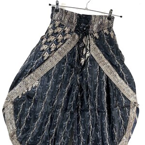 May include: Black and gray patterned palazzo pants with a lace-up waist. The wide-leg pants feature a decorative border and are hanging on a metal hanger. The fabric has a subtle floral design.