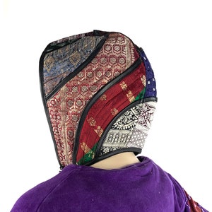 May include: A hooded head covering made from colourful patterned fabric. The fabric is sewn together in a geometric pattern. The hood is lined with black fabric.