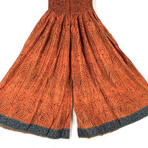 May include: Orange wide-leg pants with a patterned design and a green and burgundy trim. The pants have an elastic waistband.