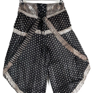 May include: Black palazzo pants with a white polka dot pattern. The pants have a wide leg design and are trimmed with a silver and gold patterned border. The pants are hanging on a hanger against a white background.