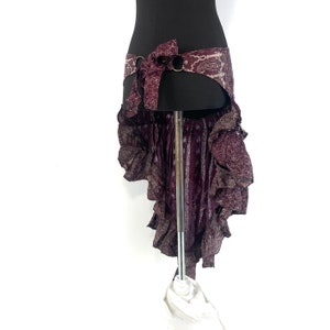 May include: A burgundy and white patterned skirt with a ruffled hem and a matching patterned belt with a metal buckle. The skirt is on a mannequin.