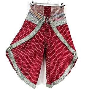 May include: Red palazzo pants with a vertical stripe pattern and a decorative border. The waistband features a patterned fabric with a lace-up back. The pants have a wide leg design and are hanging from a metal hanger.