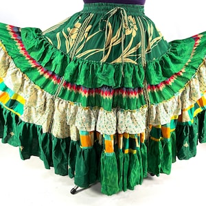 Puede incluir: Una falda verde de múltiples capas con estampado floral y ribetes de colores. La falda tiene un dobladillo con volantes y está hecha de una tela ligera.