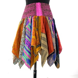 May include: A colorful patchwork skirt with a pink elastic waistband. The skirt is made of various fabrics with floral and geometric patterns.