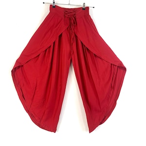 Puede incluir: Pantalones rojos de pierna ancha con un detalle de encaje en la cintura y una abertura en la parte delantera.