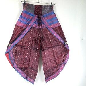 May include: Wide-leg, patterned pants in shades of burgundy, blue, and teal. The pants feature a high waist with a lace-up detail and decorative buttons. The fabric has a subtle sheen, and the design includes geometric and floral patterns.