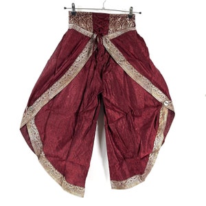 May include: Burgundy harem pants with gold trim and a decorative waistband. The pants have a wide, flowing design with a lace-up detail at the waist. The gold trim is intricately patterned, adding a touch of elegance to the garment.