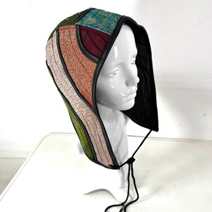 May include: A multi-coloured quilted hooded hat with a black leather trim. The hat is made of a variety of fabrics, including green, pink, brown, and blue.