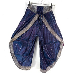 May include: Wide-leg, blue pants with a shimmering, silky texture. The pants feature a decorative silver and gold trim along the edges and waist. A drawstring closure is visible at the waist, and the pants are hanging on a black hanger.