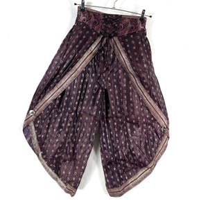 May include: Wide-leg, dark purple pants with a paisley patterned waistband and a decorative lace-up detail. The pants feature a repeating floral pattern and are trimmed with a metallic border. They have a unique wrap-around design with button closures.
