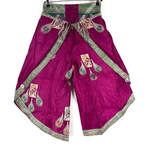 May include: Magenta-colored palazzo pants with a decorative embroidered design. The pants feature a lace-up back and a wide-leg design. The edges are trimmed with a silver and green border. The pants are hanging on a black hanger against a white background.