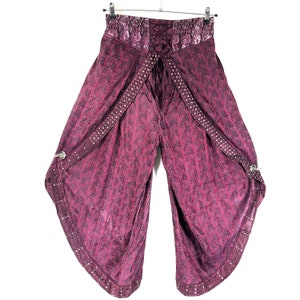 May include: Burgundy palazzo pants with a patterned design and a lace-up waist. The pants have decorative straps with white dot accents and silver-toned hardware. The fabric has a subtle sheen, and the pants are hanging on a metal hanger.