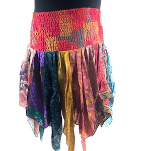 Puede incluir: Falda de patchwork colorida con una cintura ancha y elástica. La falda presenta una variedad de telas vibrantes en tonos de rojo, naranja, morado, verde y dorado. La falda tiene un dobladillo asimétrico y fluido.