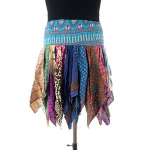 May include: A colorful, patchwork skirt with a turquoise elastic waistband. The skirt is made of various patterned fabrics in shades of blue, purple, green, and gold. The skirt is displayed on a metal stand.