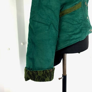 May include: A green corduroy jacket with a lace trim on the sleeves and a pocket. The jacket has a black lining and a button closure.