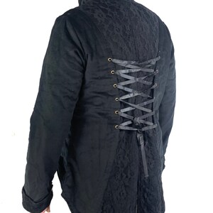 May include: Black long-sleeved jacket with a lace back panel and a corset-style lacing detail. The jacket has a high collar and a long, pointed tail.
