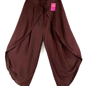 May include: A pair of brown palazzo pants with a unique wrap-around design. The pants feature a lace-up detail at the waist and a flowing, wide-leg silhouette. The fabric has a slight sheen, and the pants are hanging from a hanger.