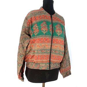 May include: A green, orange, and brown patterned bomber jacket with a zipper closure. The jacket has a paisley design on the sleeves and a floral pattern on the body.