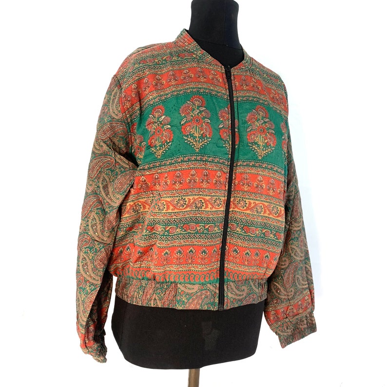 May include: A green, orange, and brown patterned bomber jacket with a zipper closure. The jacket has a paisley design on the sleeves and a floral pattern on the body.