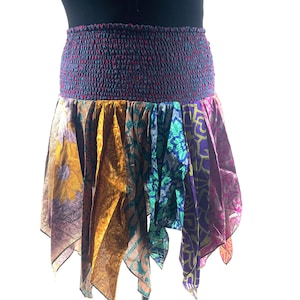 May include: A patchwork skirt with a smocked waistband. The skirt is made from panels of patterned fabric in purple, gold, teal, and pink. The skirt has an asymmetrical hemline and is designed to be worn at the waist.