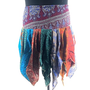 May include: A patchwork skirt with an elasticated waistband. The skirt is made from panels of patterned fabrics in blue, red, orange, and green. It has an asymmetrical hemline and a bohemian design. The skirt is a vibrant piece of clothing.