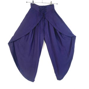 Puede incluir: Un pantalón palazzo de color púrpura oscuro con cintura alta y detalle de cordones en la espalda. Las perneras anchas caen abiertas, creando una silueta fluida. El pantalón está colgado de una percha metálica sobre un fondo blanco.