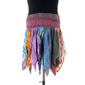 Peut inclure: Jupe patchwork colorée avec une large ceinture élastique. La jupe présente une variété de tissus à motifs dans les tons de bleu, violet, orange et vert. La jupe est présentée sur un support sur fond blanc.
